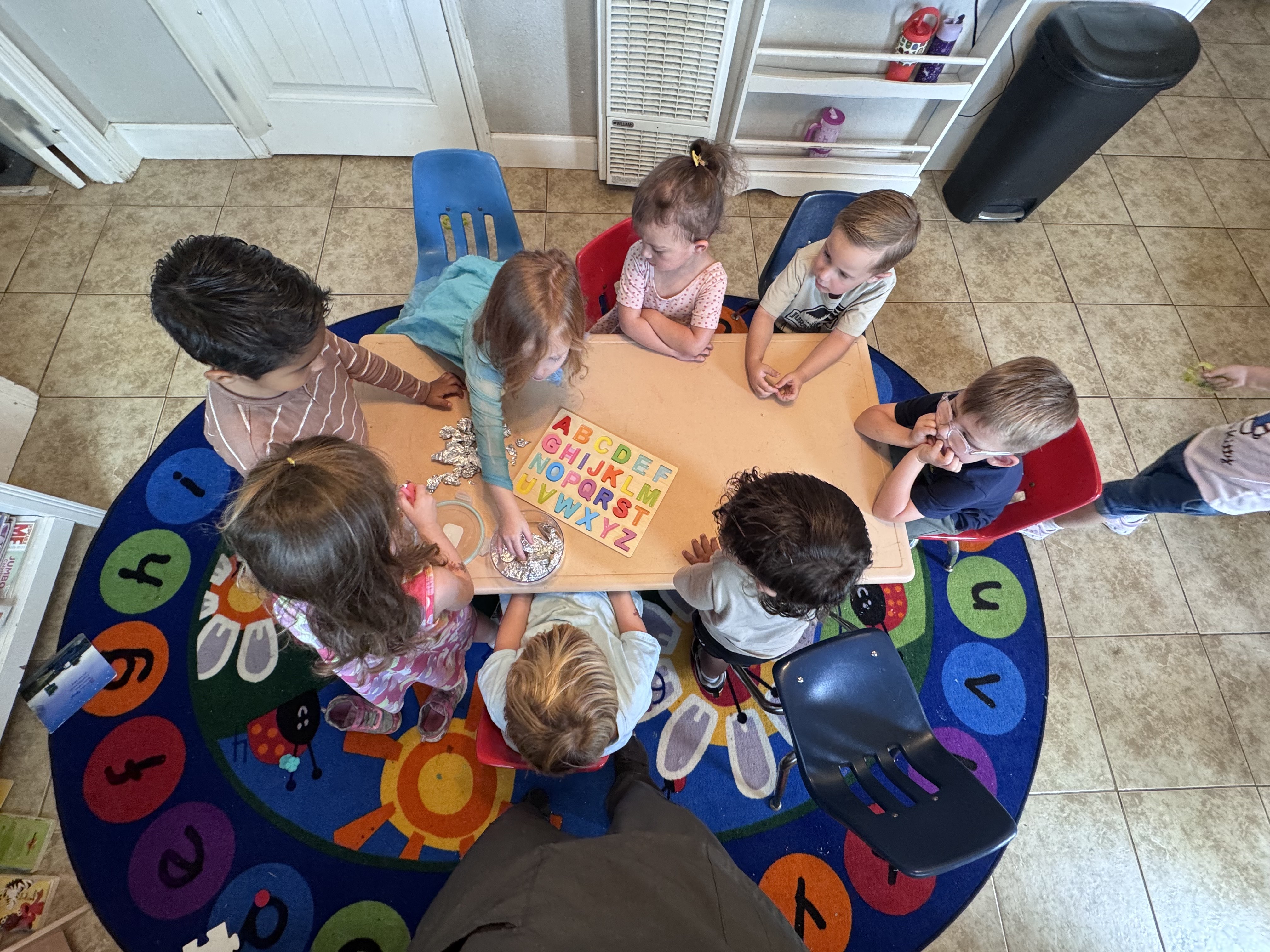 Preschoolers gathered around a table with a colorful alphabet puzzle
