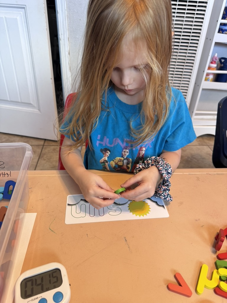 Preschooler matching a green letter chip to a sunny picture-word card
