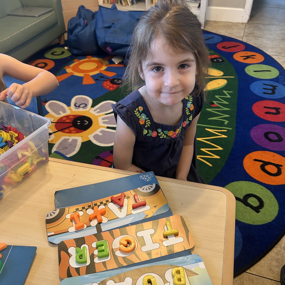 Smiling girl playing with letter puzzles at a preschool table