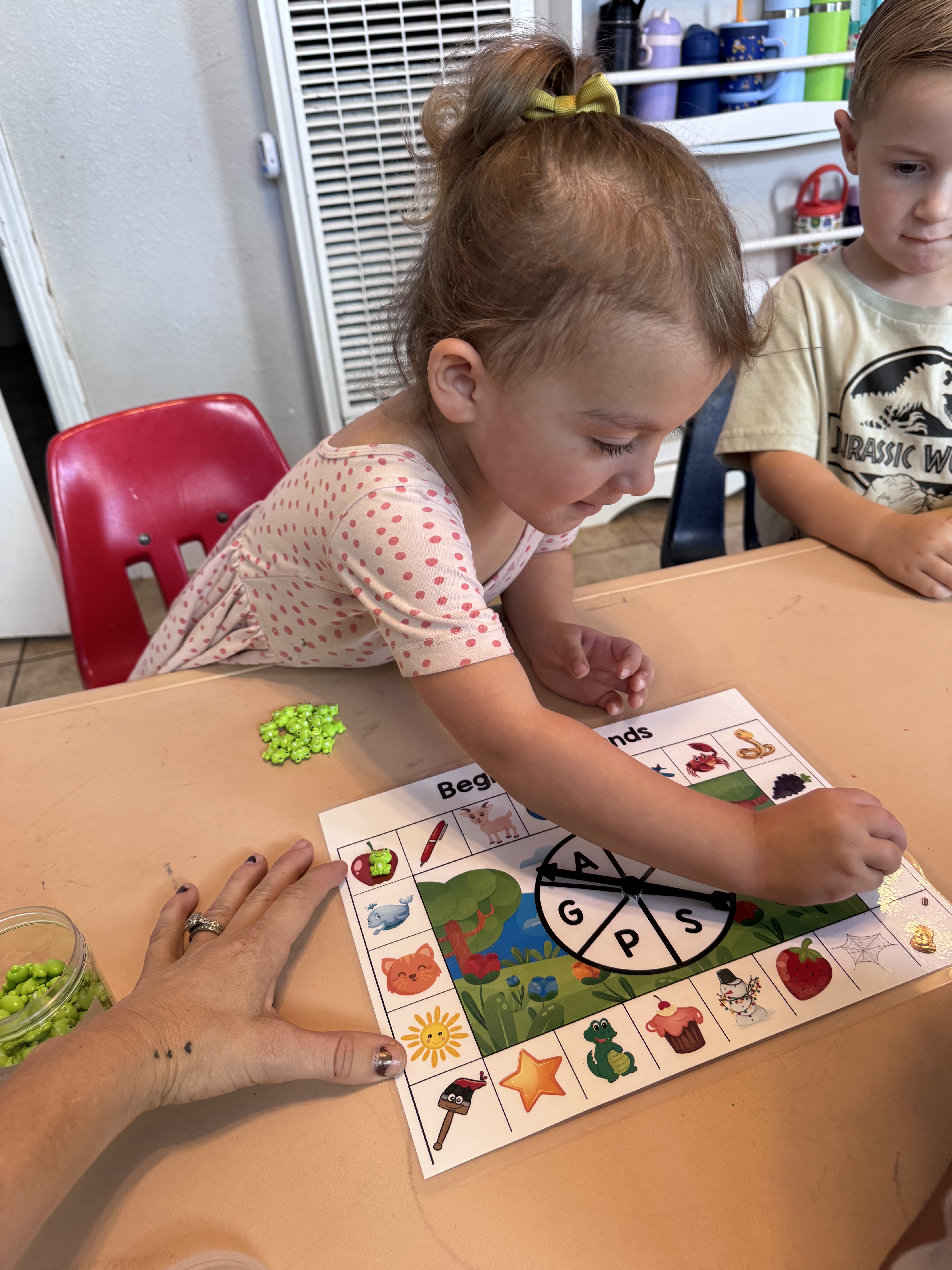 Toddler giving the spinner a whirl on a beginning-sounds game board while a friend watches