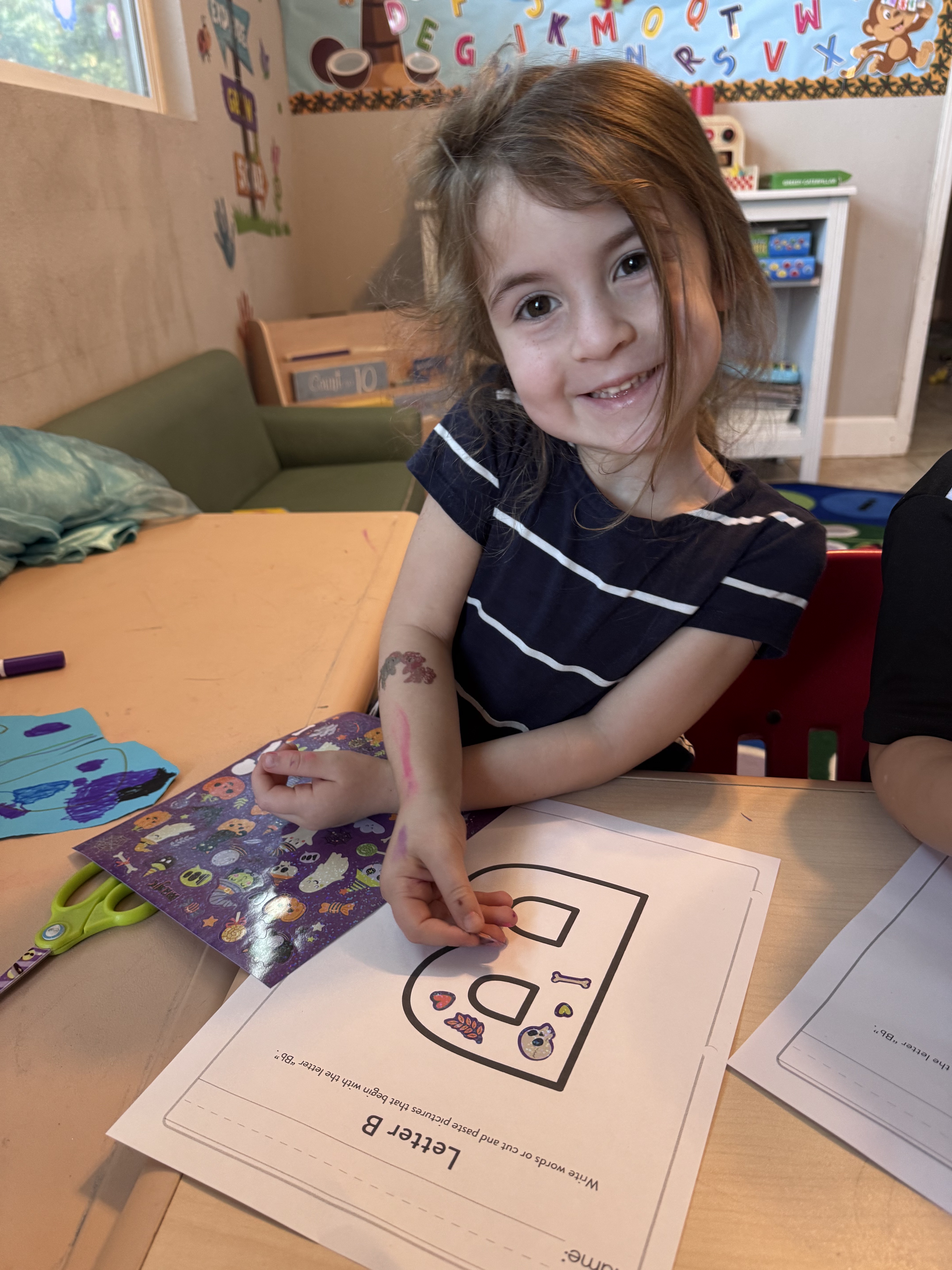 Smiling preschooler decorating her Letter B craft with Halloween stickers