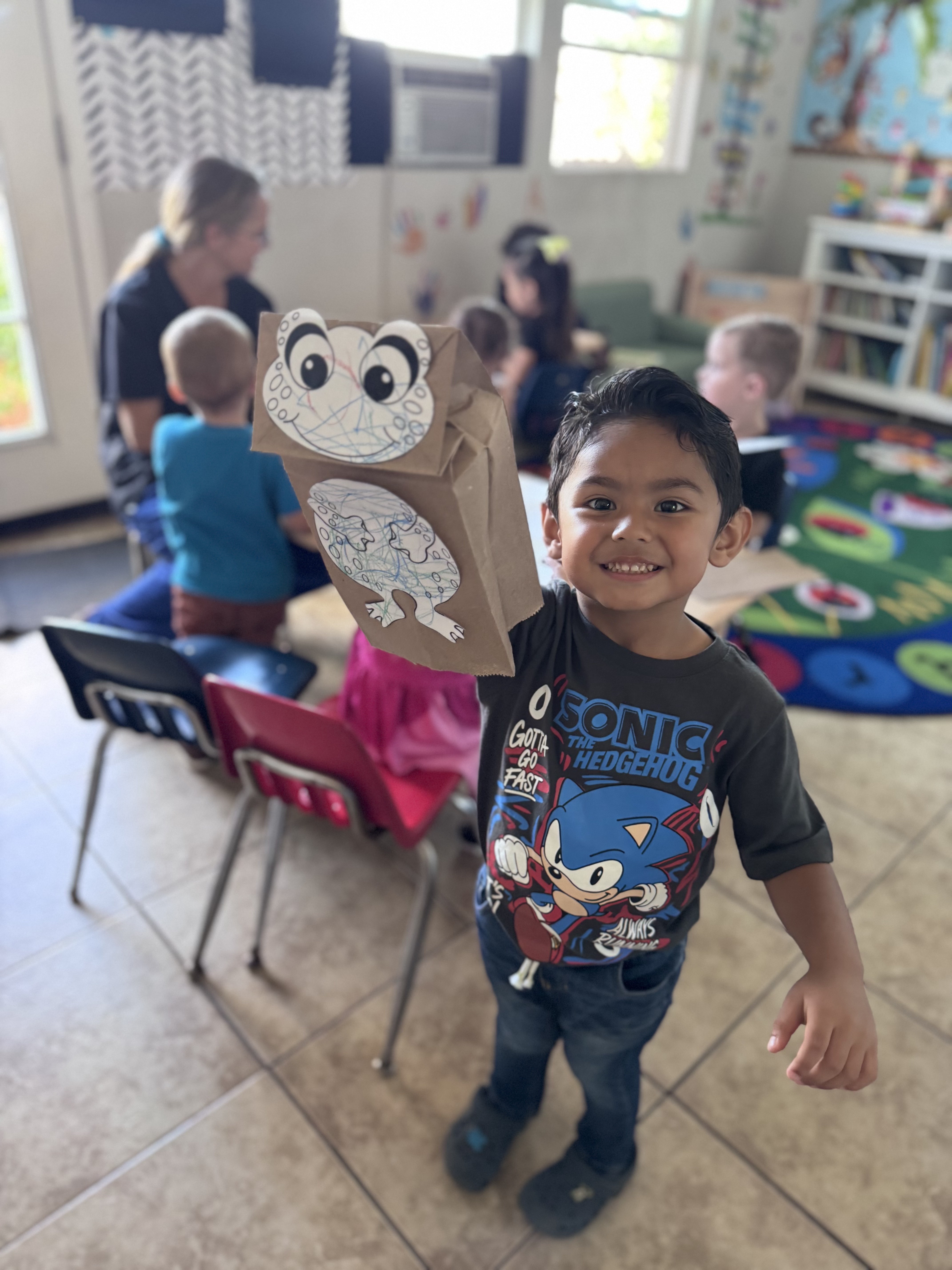 Preschooler proudly holding up his paper-bag frog puppet craft