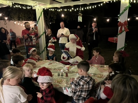 Santa sharing a storybook with the children at the outdoor Christmas party under the string lights
