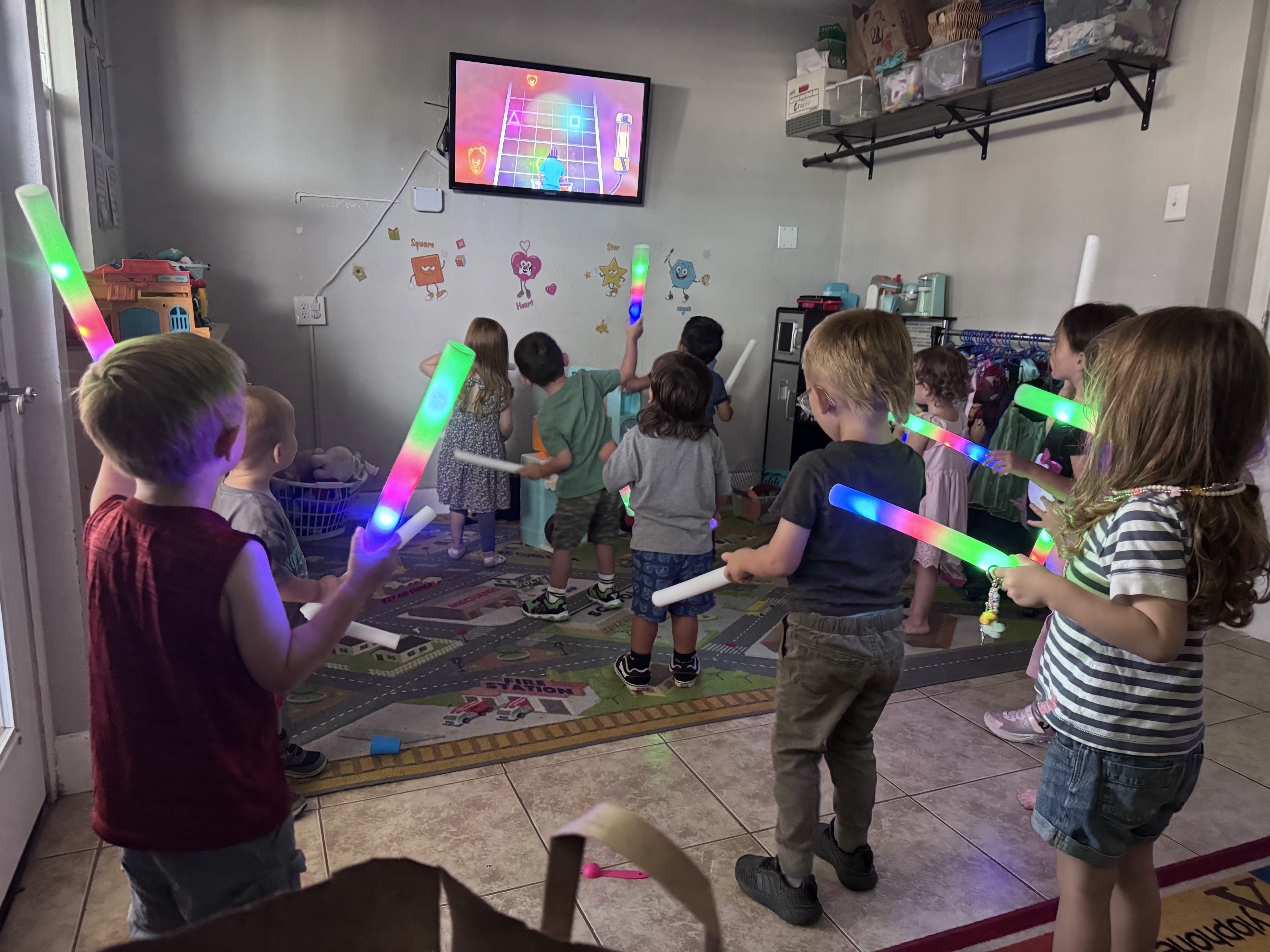 Preschoolers dancing with glowing light-up batons in front of the classroom TV
