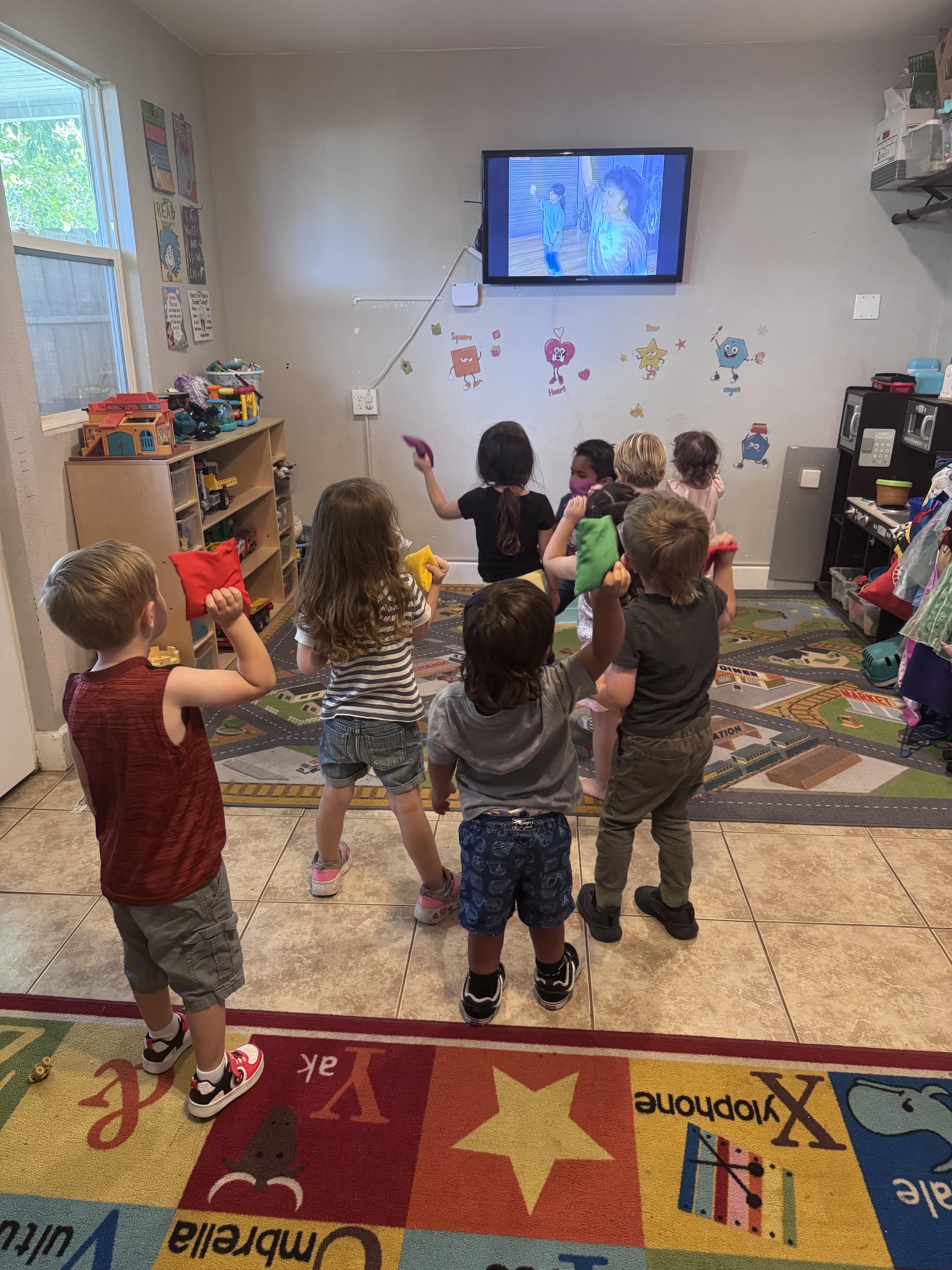 Preschoolers dancing with colorful beanbags during a music video in the classroom