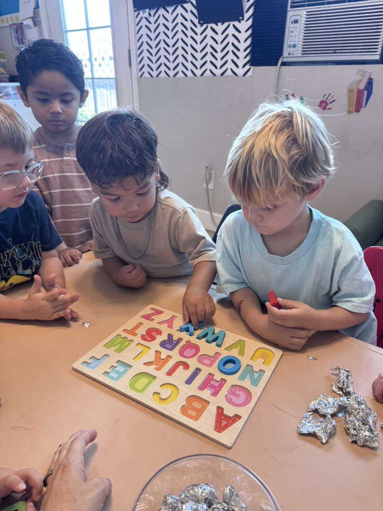 Preschoolers gathered around the table matching letters on a wooden alphabet puzzle board