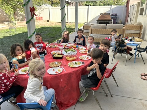 Preschoolers enjoying a holiday feast around the red party table in the backyard