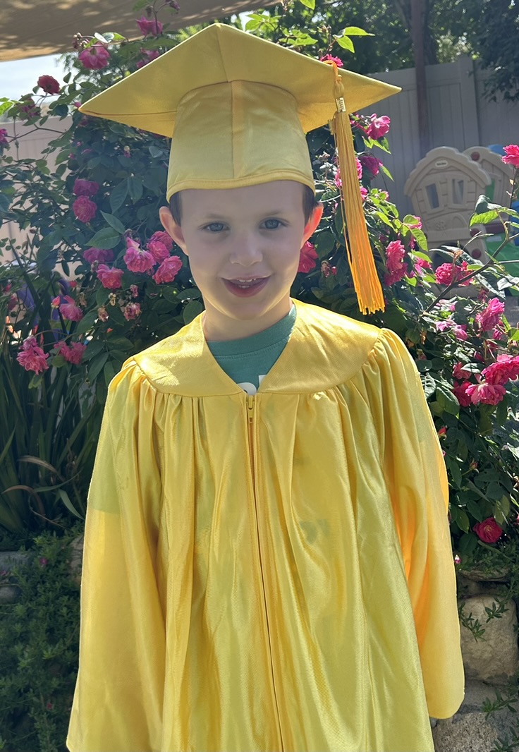 Smiling boy graduate in a yellow cap and gown in front of the rose garden