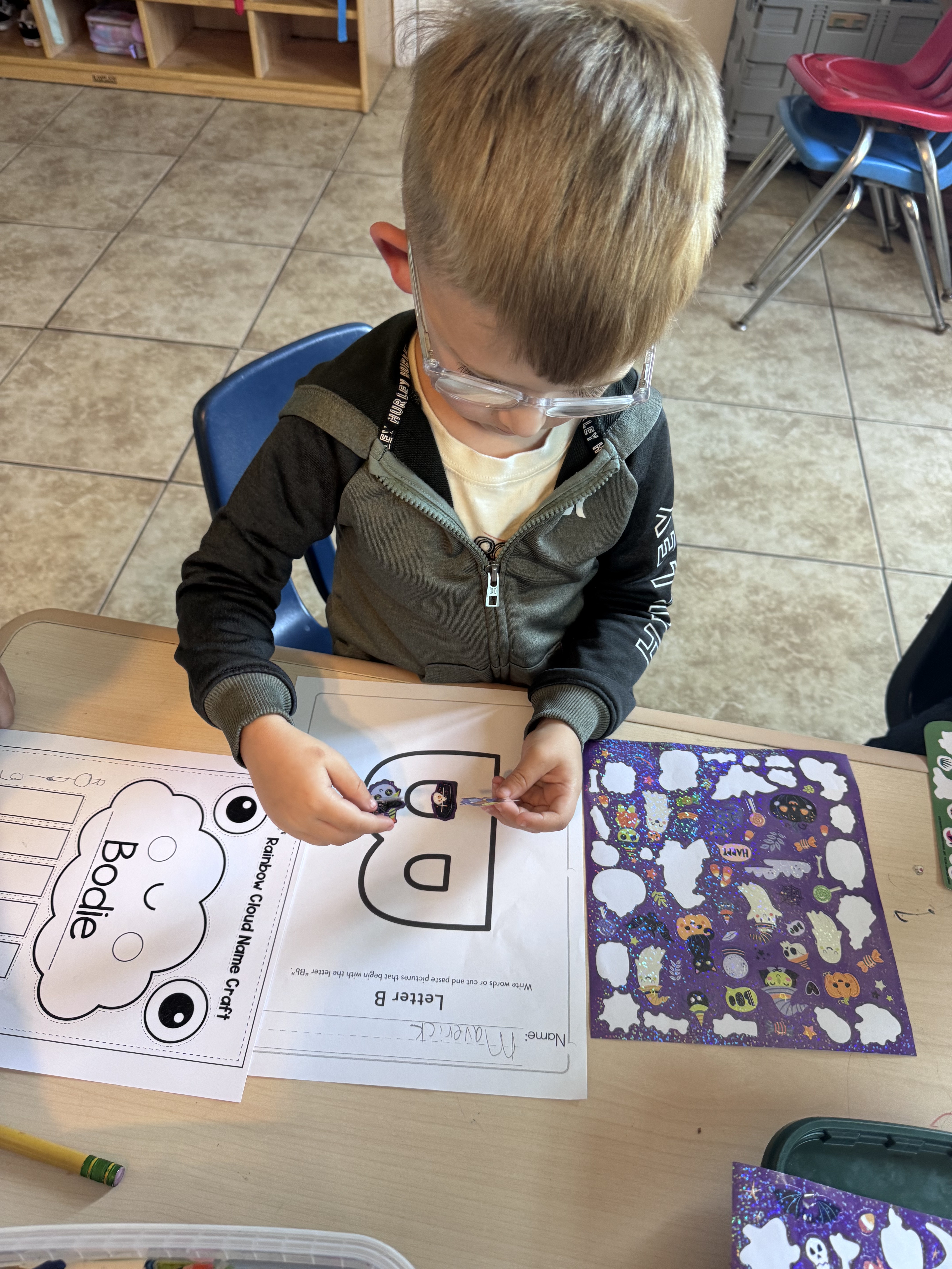 Preschooler gluing Halloween stickers on a Letter B craft worksheet