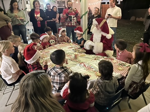 Children in Santa hats gathered around the party table to visit Santa while parents watch