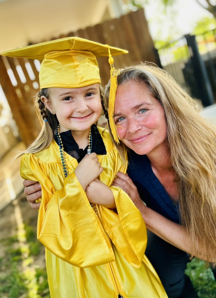 Miss Robin smiling beside a preschool graduate in a yellow cap and gown