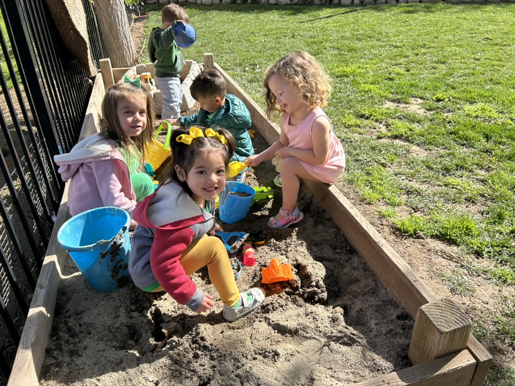 Preschoolers playing with buckets and shovels in the sandbox on the grass