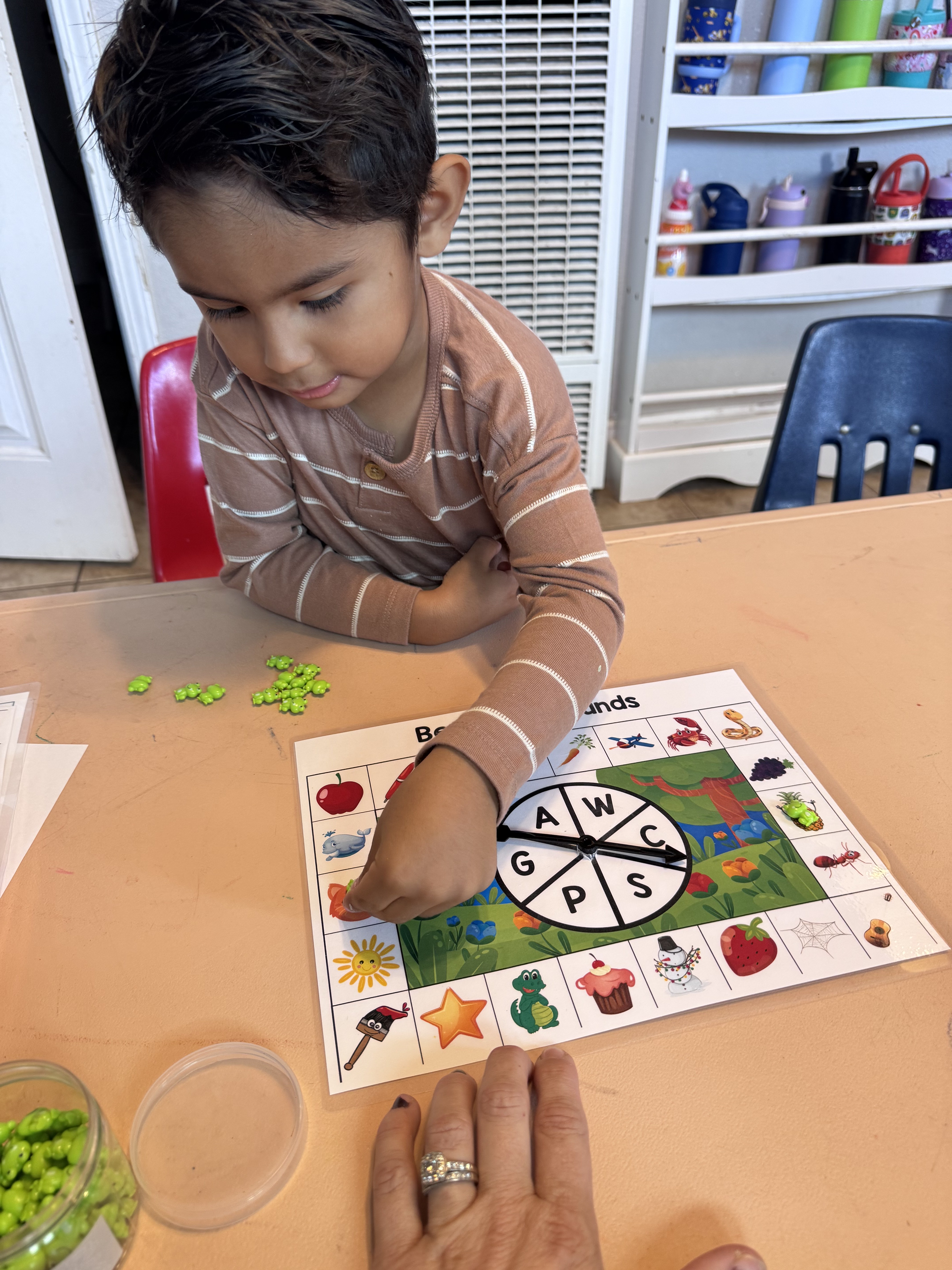 Preschooler playing a beginning-sounds board game with a spinner and frog counters